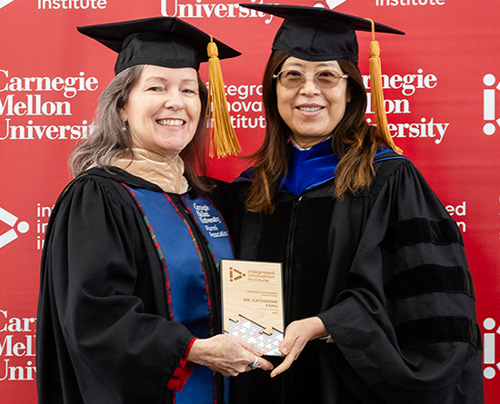 Two women in graduation gowns holding an award